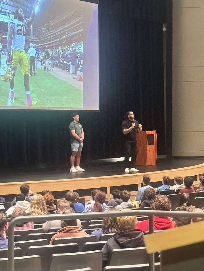 Alex Green speaking on an auditorium stage with students in the audience