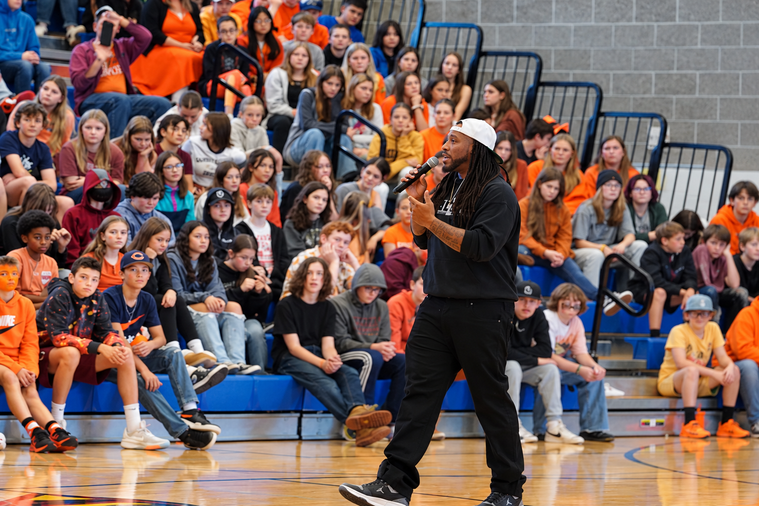 Alex Green speaking in front of students seated in gym bleachers